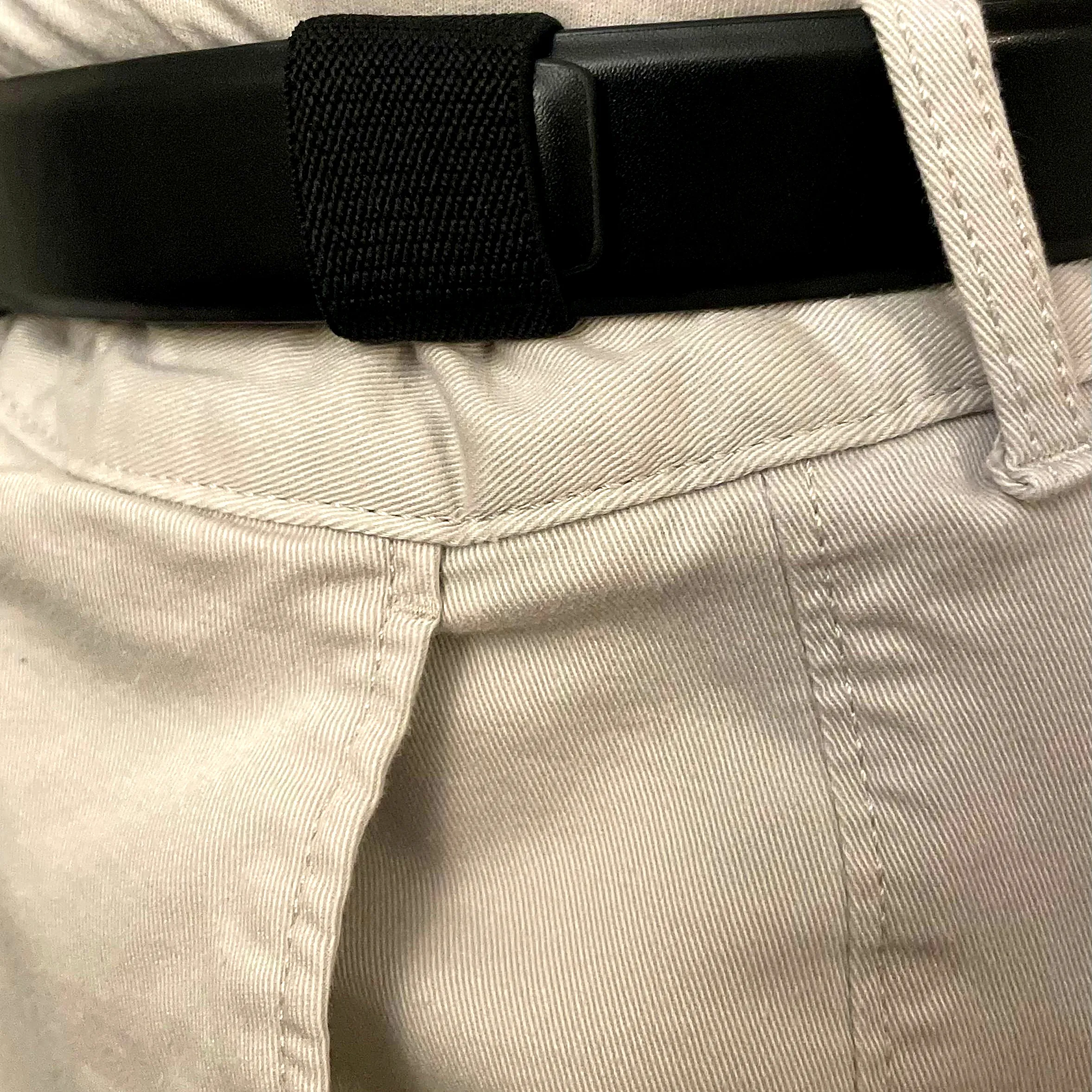 Looped holding the loose end of a black belt flat against khakis